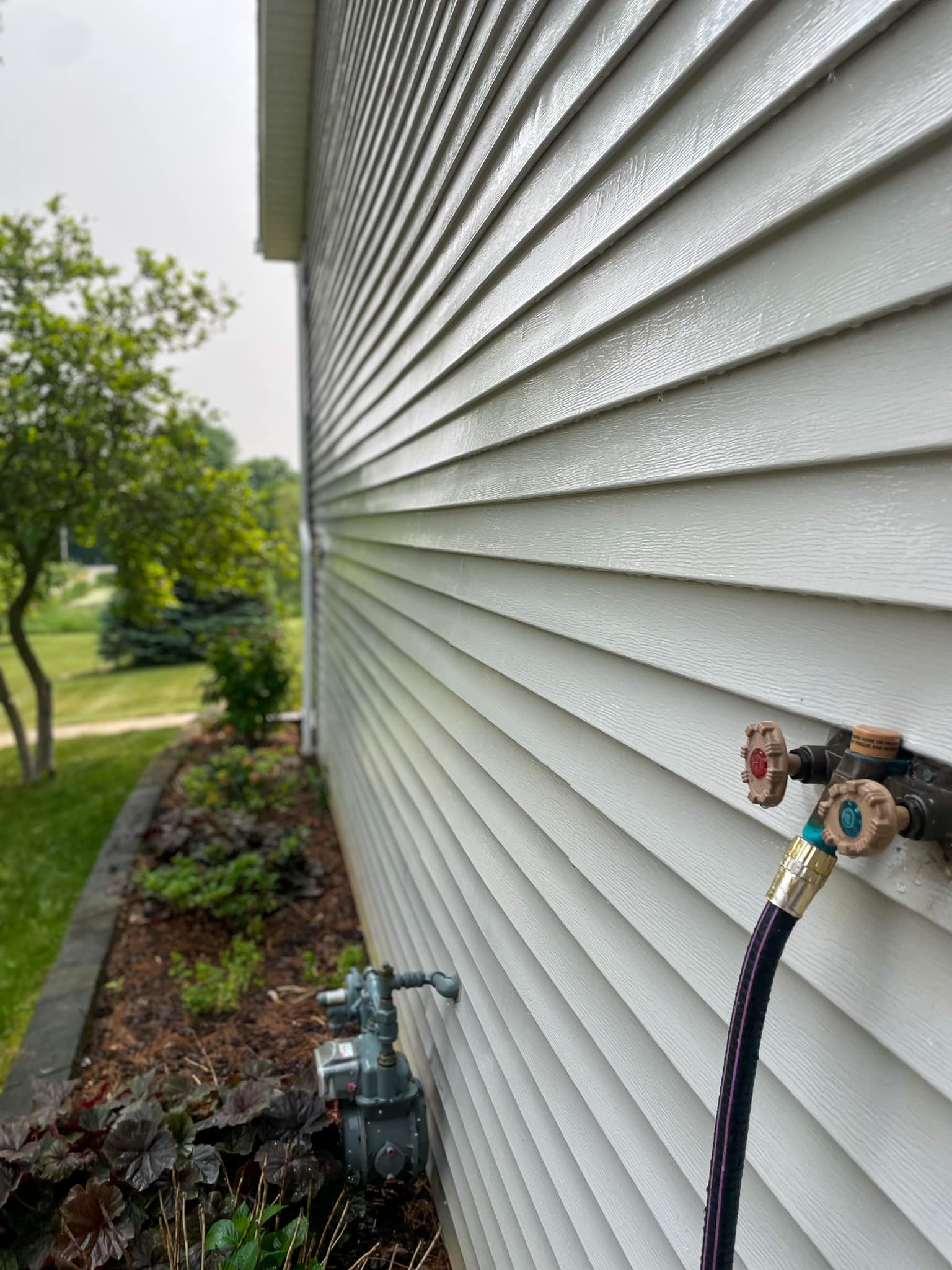 Vinyl siding on a Champaign County home being soft-washed — hose and equipment visible along the foundation